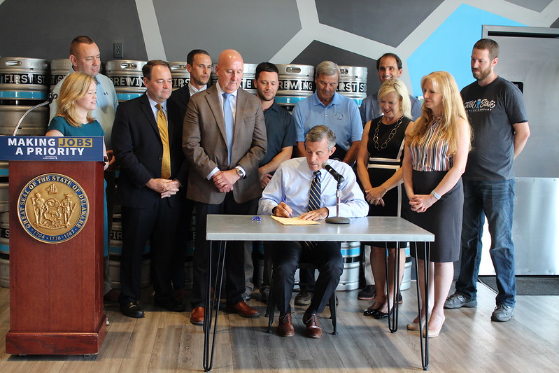 Governor Carney signs legislation in front of a group at First State Brewing