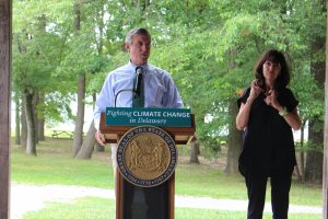 Governor Carney stands at the podium at a bill signing. An ASL interpreter stands to his left. The podium sign reads "Fighting climate change in Delaware." 